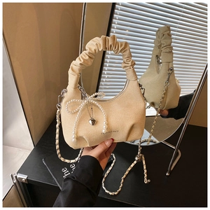 Detail of beige pleated cloud bag with pearl bow and heart charm on mirror surface