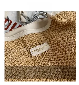 Close-up of woven straw texture with leather logo patch and silver chain strap details