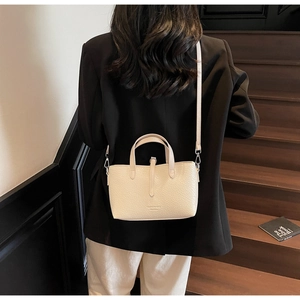 Detailed side view of beige textured leather crossbody bucket bag on female model