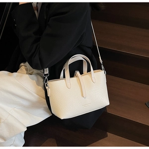 Detail of cream white textured faux leather handbag showing dual handles and shoulder strap