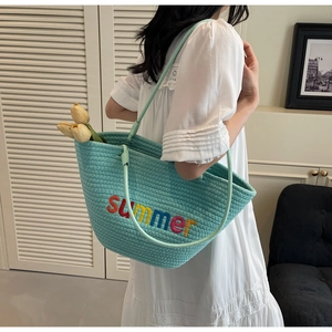 Detail of mint green woven tote bag featuring colorful summer embroidery and slim straps