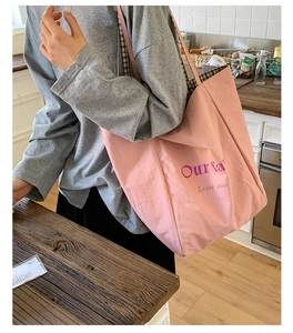 Pink tote bag with plaid lining and purple graphic text shown in a cozy home setting