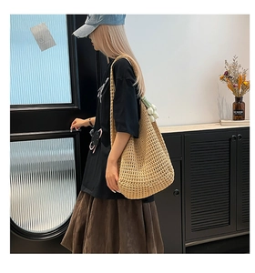 Detail of hand-crocheted hollow cotton mesh shoulder bag with a white tulip charm accessory