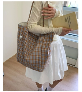 Detail of a large brown checkered canvas tote bag with side label in a cozy home setting