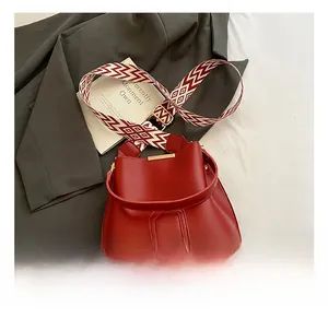 Macro shot of a red bucket bag featuring a polished surface and a woven shoulder strap