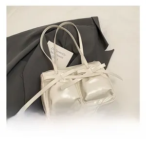 Detail of a vintage-style beige underarm bag featuring decorative ribbons and dual pockets