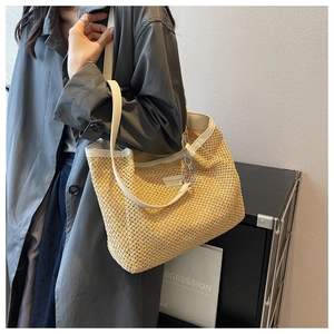 Detail of a beige woven straw tote bag with white leather straps and metallic chain link