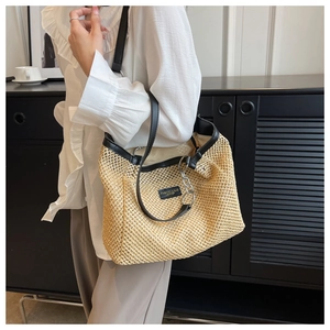 Straw woven tote bag with black leather straps and silver chain detail worn by a model