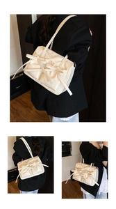 Detail of a creamy white underarm bag with a large bow and glossy finish