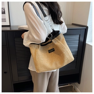 Detail of straw tote bag showing black leather trim, metal chain strap and woven texture