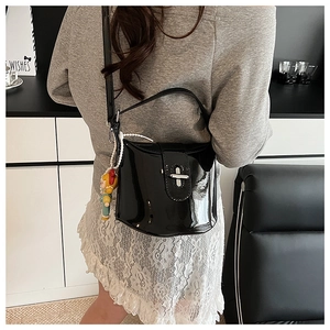 Dettaglio di una borsa a secchiello in vernice nera con chiusura a scatto e ciondolo bambola