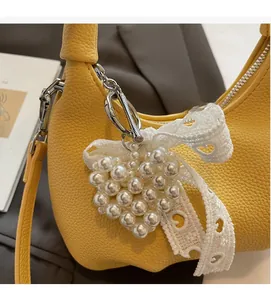Detail of yellow lychee leather handbag featuring a heart pearl pendant and lace bow accessory