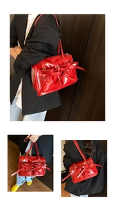 Detail view of red glossy underarm bag featuring bow accents and pleated leather texture