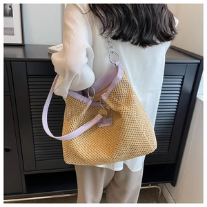 Close-up of woven straw tote bag featuring lavender leather handles and metal chain detail