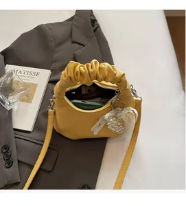 Detail of yellow ruched handle handbag with pearl lace bow charm on grey blazer backdrop