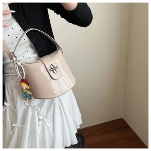 Dettaglio borsa a secchiello in vernice beige con chiusura girevole in metallo e manico