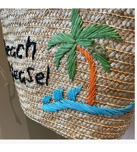 Detail of hand-woven straw bag featuring colorful beach palm tree embroidery and Beach text