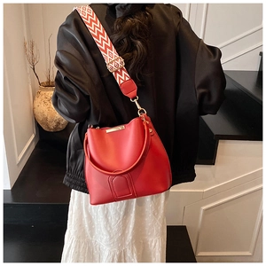 Close-up of red patent leather bucket bag featuring a geometric patterned woven strap