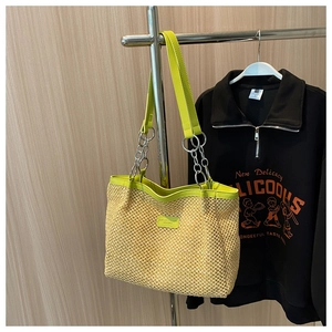 Detail of summer straw tote bag featuring bright green leather handles and silver chain links