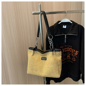 Detail of a large woven straw tote bag with black leather trim and chain shoulder strap
