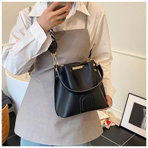 Detail of black leather bucket bag featuring wide geometric strap and gold metal hardware