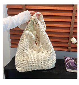 Detail of hollow-out knit crochet tote bag with decorative 3D tulip charm and woven texture