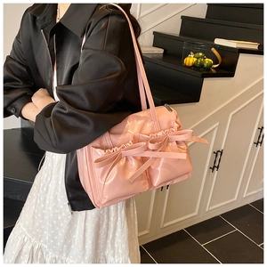 Close-up of pink patent leather shoulder bag with decorative bows and pleated texture