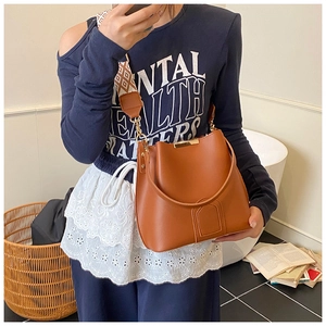 Brown leather bucket bag with geometric strap shown on model in cozy interior scene