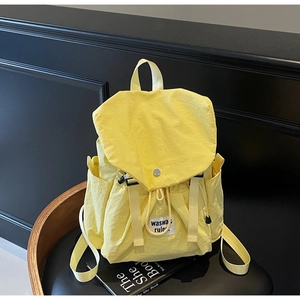 Detail of a bright yellow nylon backpack with drawstring closure and silver buckle on a chair