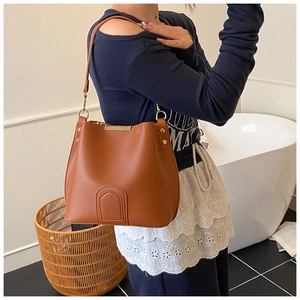 Detailed close-up of brown bucket bag with gold circular metal buckles and wide strap