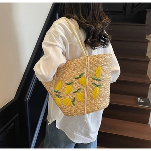 Detailed view of handmade straw bag featuring vibrant yellow lemon embroidery and dual straps