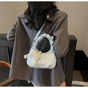 Detail of light blue crescent bag with pleated handle, pearl heart charm and lace bow