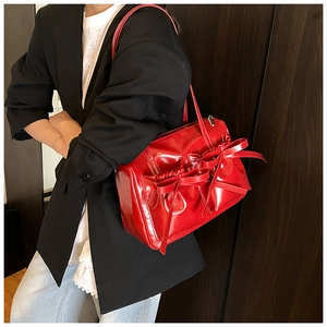Detail of red patent leather shoulder bag with large decorative bows on a model