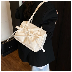 Close-up of beige glossy tote bag with large bows and pleated edge details