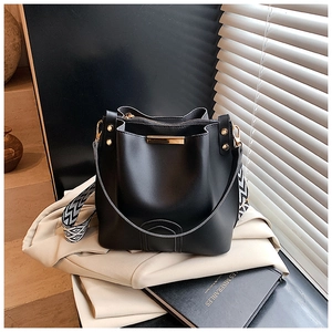 Close-up of black leather bucket bag with gold metal trim and geometric woven strap