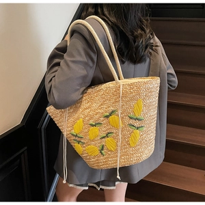 Close-up of a large straw tote bag featuring yellow lemon embroidery and rope handles