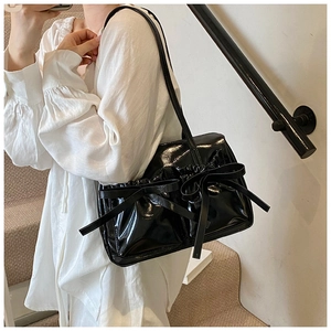 Close-up of a black glossy shoulder bag featuring a large bow and pleated ruffled edges