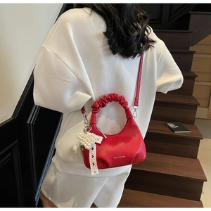 Detail of red textured leather crescent bag with pleated handle and pearl heart charm
