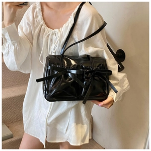 Close-up of black glossy patent leather shoulder bag with chic pleated bow detail