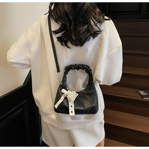 Detail of black pebbled leather handbag with pearl heart and lace bow on wooden stairs