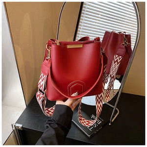 Detail of red bucket bag featuring a wide geometric woven strap and gold metal hardware