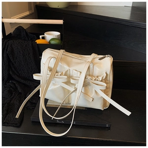 Detailed view of cream-white bow shoulder bag with pleated texture and top zipper
