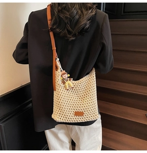 Detail of hand-woven beige bucket bag with brown leather strap and cute doll pendant