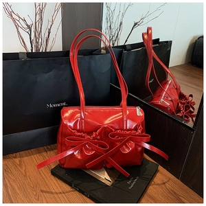 Detailed view of glossy red handbag with double bows and zip closure in a mirrored setting