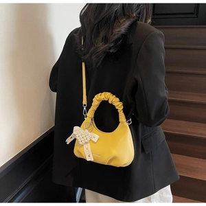 Detail of yellow pleated handbag with pearl lace bow charm on black suit backdrop