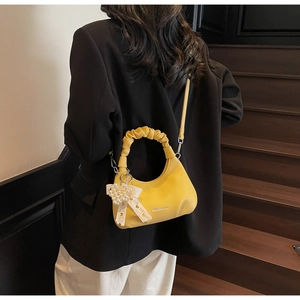Macro shot of yellow pleated handle handbag with pearl heart and lace bow charm detail