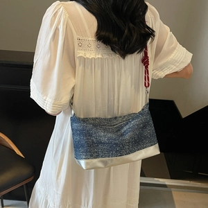 Blue denim underarm bag with silver base and red knotted shoulder strap detail on model
