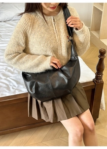 Minimalist black pleated crescent bag shown on shoulder in a warm interior setting