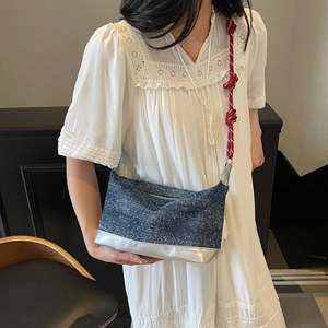 Detail view of denim shoulder bag with red-white braided rope strap on white lace dress