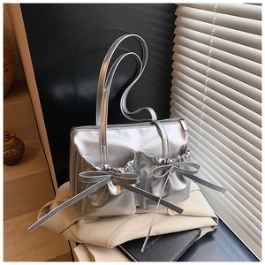 Detailed close-up of metallic silver shoulder bag featuring decorative bow and utility pockets